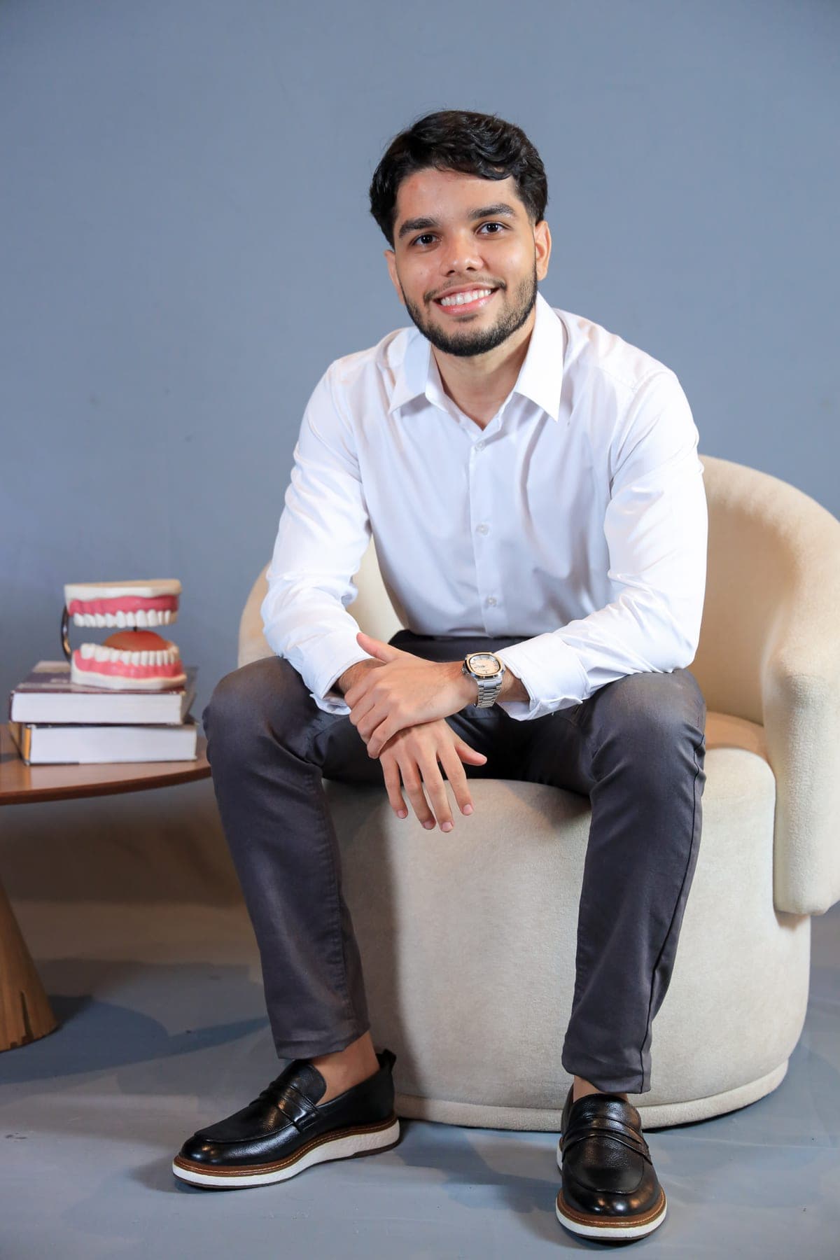 Dr. Samuel Souza sentado em poltrona ao lado de modelos de arcada dentária