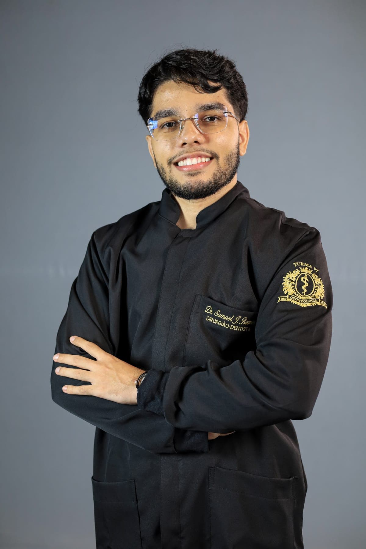 Dr. Samuel Souza, cirurgião-dentista, de jaleco e braços cruzados